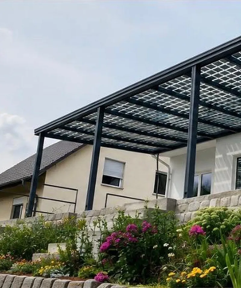 Pergola en verre solaire fixée à la façade : poteaux anthracite et toiture de modules verre-verre.